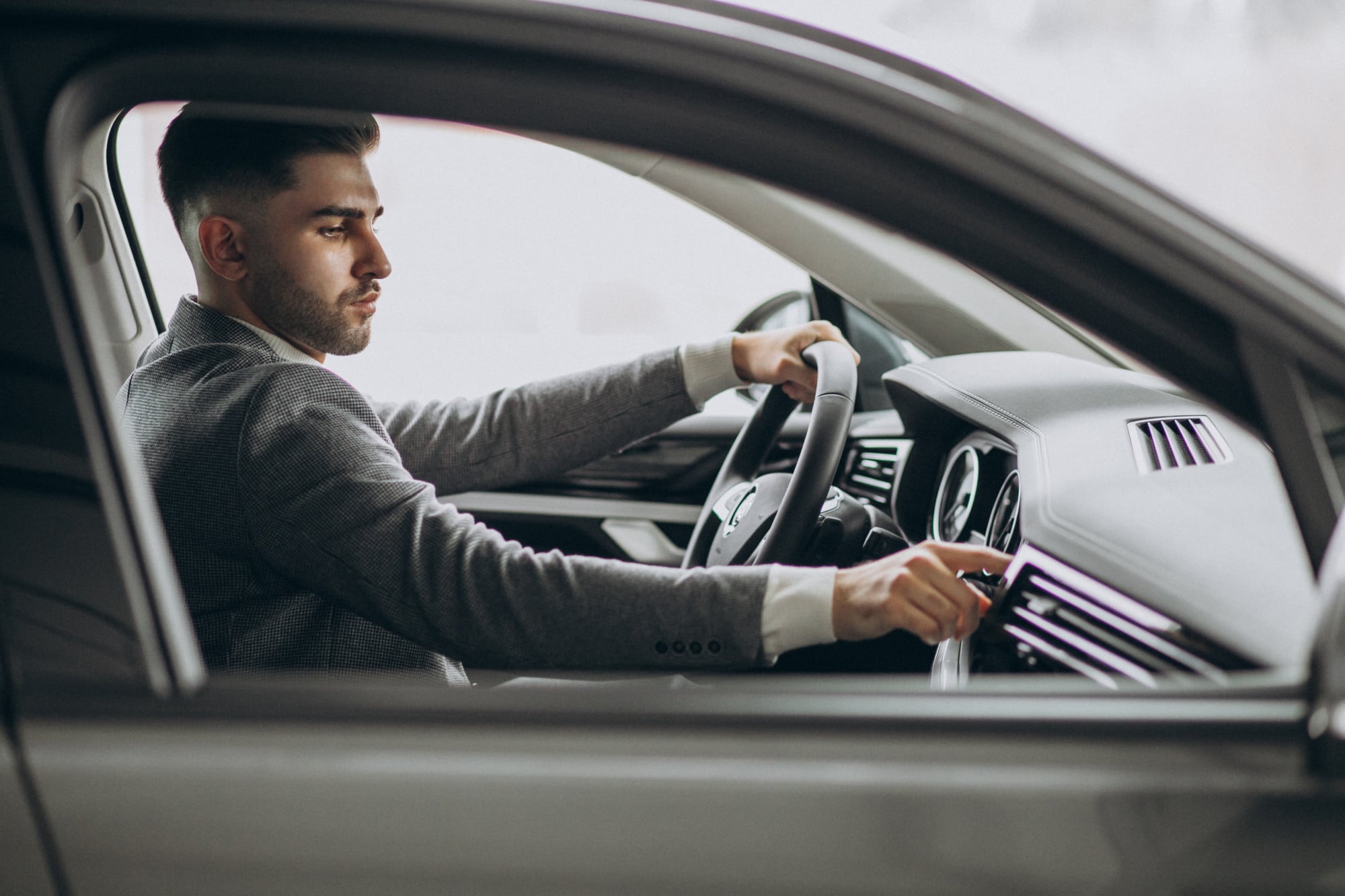 Man in suit driving, adjusting controls, appearing focused.