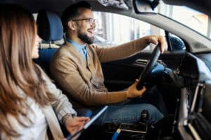 Smiling man drives car while woman in front seat holds tablet.