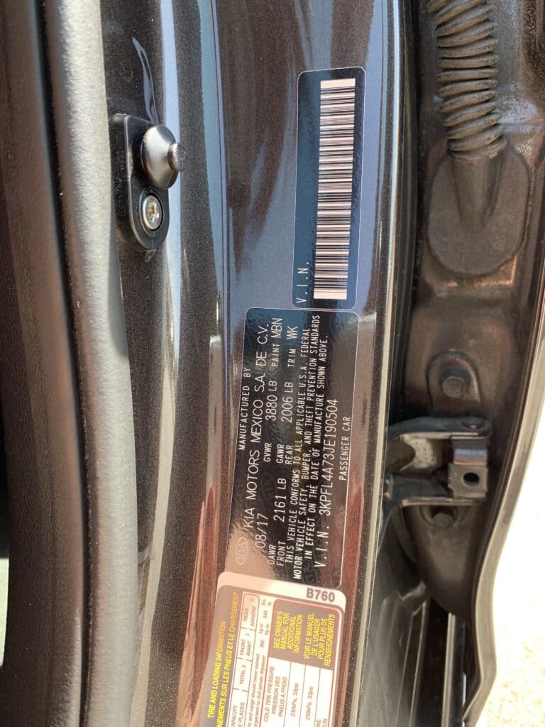 Car door frame with manufacturer sticker displaying VIN and vehicle info near hinges.