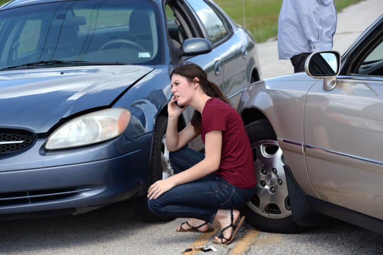 Woman crouches by crashed cars, on phone; damaged vehicles, person nearby. Woman crouches by crashed cars, on phone; damaged vehicles, person nearby.