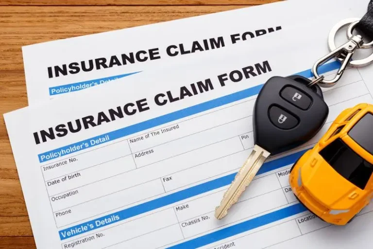 Insurance claim forms on a table with car key and yellow toy car on top.