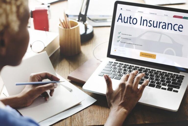 Person with pen at desk views auto insurance site on laptop, notebook nearby.