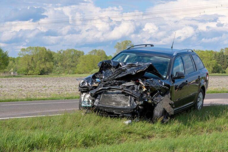 Black SUV with front-end damage on roadside by fields under partly cloudy sky. Black SUV with front-end damage on roadside by fields under partly cloudy sky.