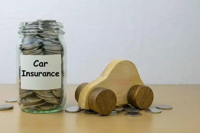 Car Insurance jar filled with coins beside a small toy car, coins spread around.