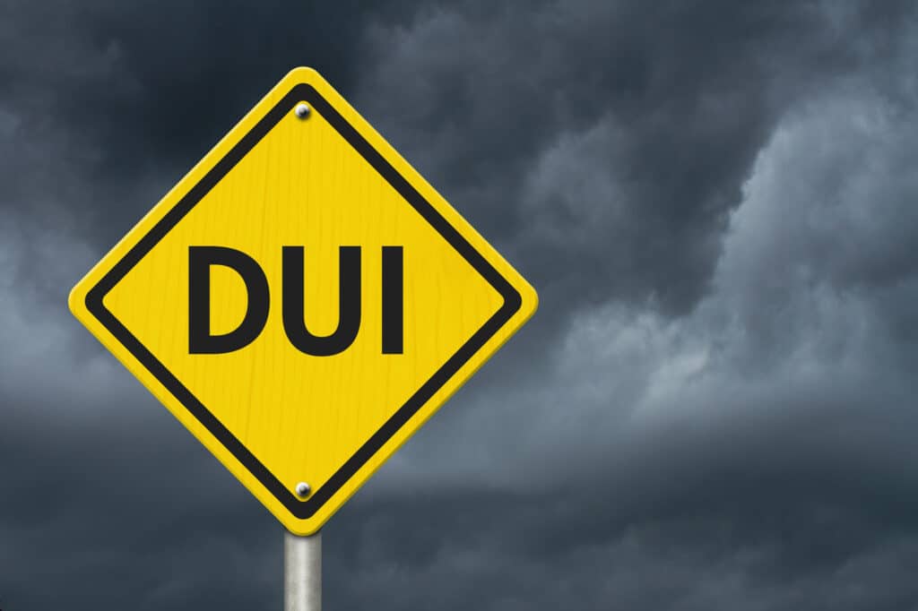 Yellow diamond DUI road sign against a dark, cloudy sky.