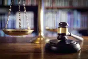 Judge’s gavel on block, brass scales and bookshelves blurred in background.