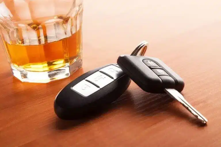 Whiskey and car keys on wood, highlighting drinking and driving risk.