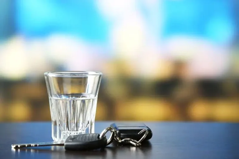 Shot glass and car keys on a dark table, background blurred.