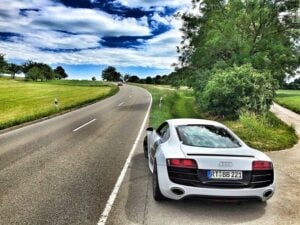 White Audi sports car parked on rural road under cloudy sky.