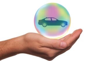 Hand holds colorful bubble with car icon, white background.