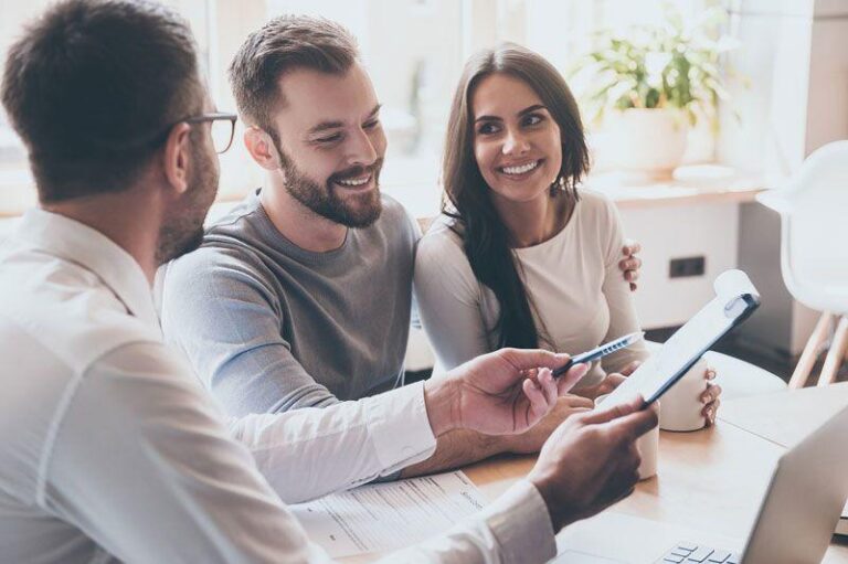 Man in glasses shows tablet to smiling couple during office consultation.