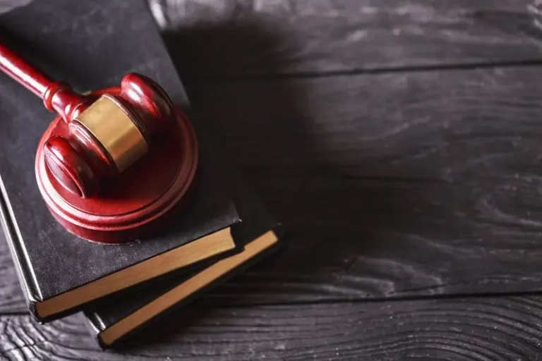 Judge’s wooden gavel on two black books on a dark wood table.