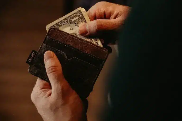 Hand placing or taking dollar bill from brown wallet.