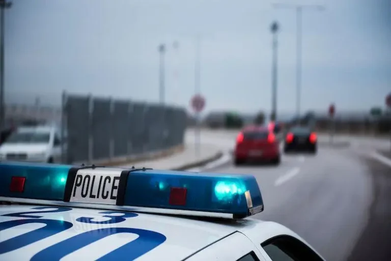 Police car with flashing blue lights parked by a curved, cloudy road.